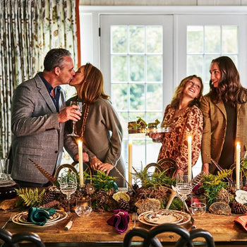 A husband and wife embrace and their children smile as they sand around the Thanksgiving table.